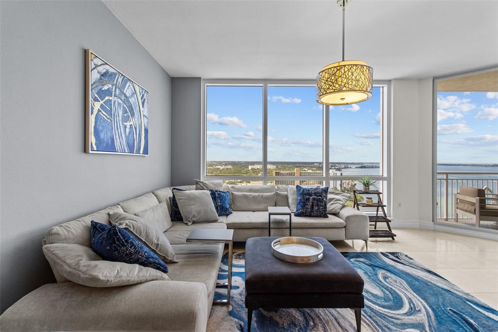 A living room features a large sectional sofa, a dark ottoman, and floor-to-ceiling windows — 331 CLEVELAND STREET UNIT 2102, CLEARWATER, FL