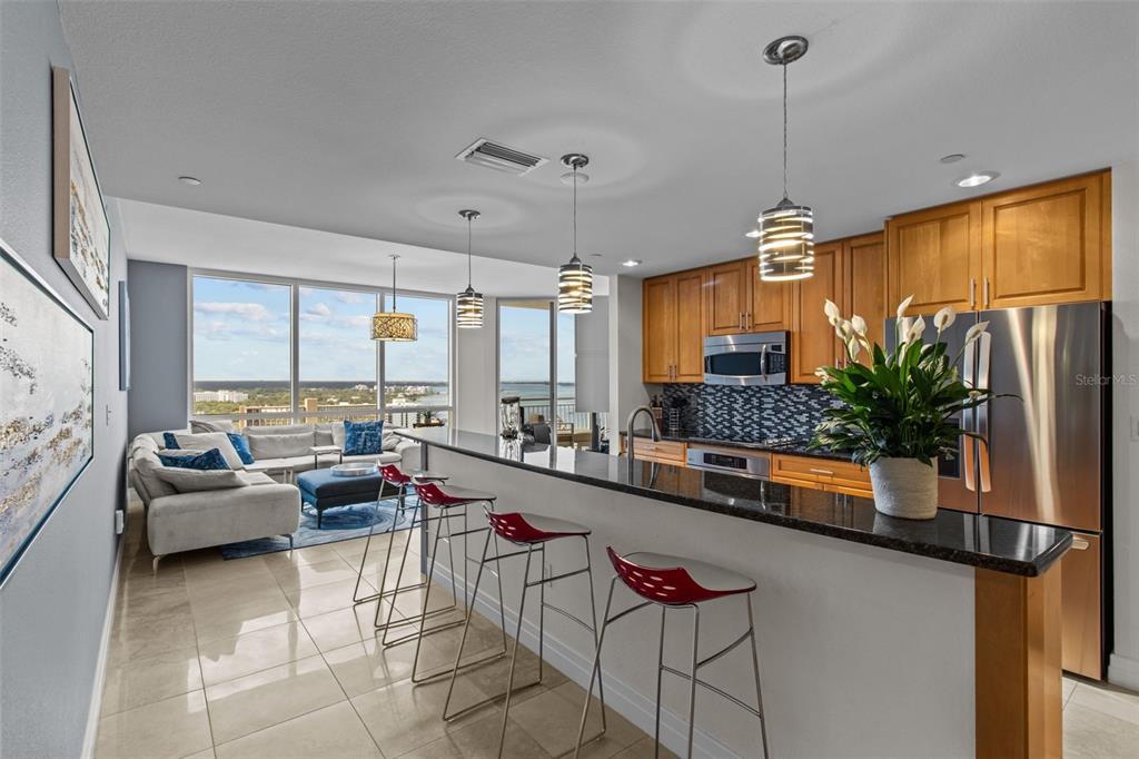 A modern kitchen with wood cabinets and a breakfast bar overlooks a living room — 331 CLEVELAND STREET UNIT 2102, CLEARWATER, FL