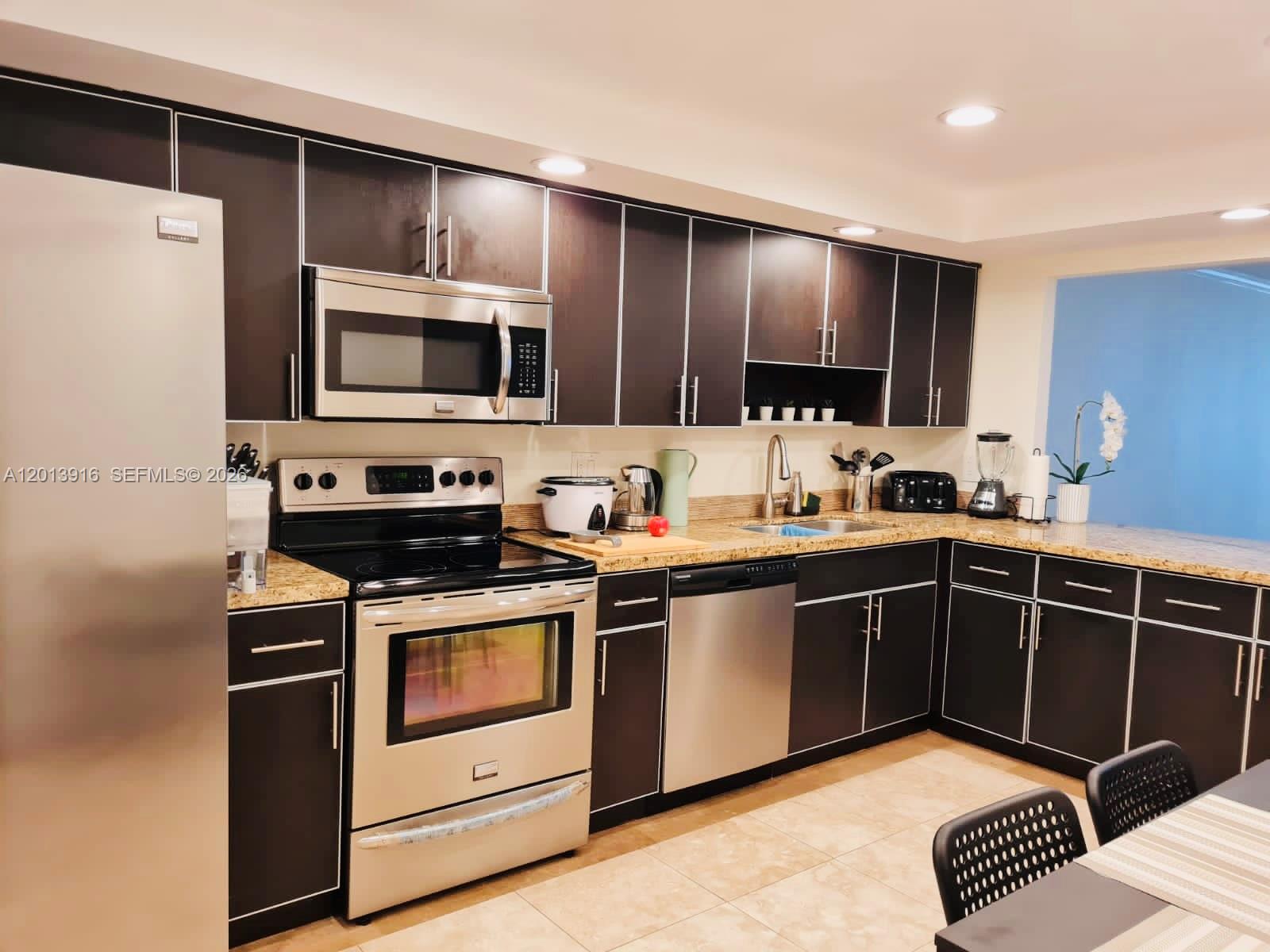 A kitchen features dark wood cabinets, stainless steel appliances, and beige granite countertops — 2500 Parkview Dr # 2114, Hallandale Beach FL 33009, HALLANDALE BEACH, FL