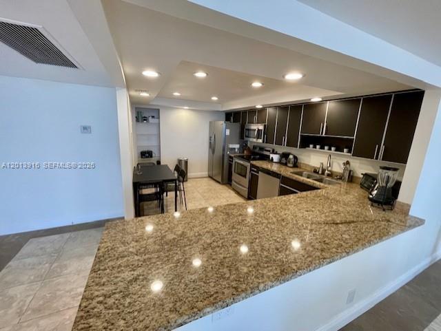 A kitchen features dark cabinetry, granite countertops, and a breakfast bar overlooking a dining area — 2500 Parkview Dr # 2114, Hallandale Beach FL 33009, HALLANDALE BEACH, FL