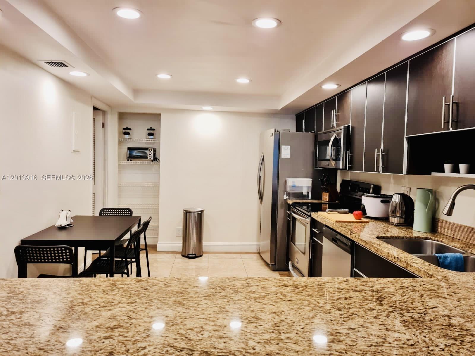 A kitchen features dark cabinetry, granite countertops, stainless steel appliances, and an adjacent dining area — 2500 Parkview Dr # 2114, Hallandale Beach FL 33009, HALLANDALE BEACH, FL