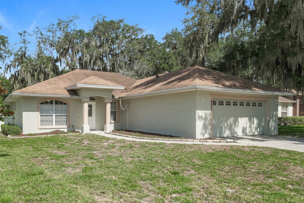 A single-story house with a beige stucco exterior, a brown roof, and a two-car garage — 6557 SHEPHERD OAKS ROAD, LAKELAND, FL