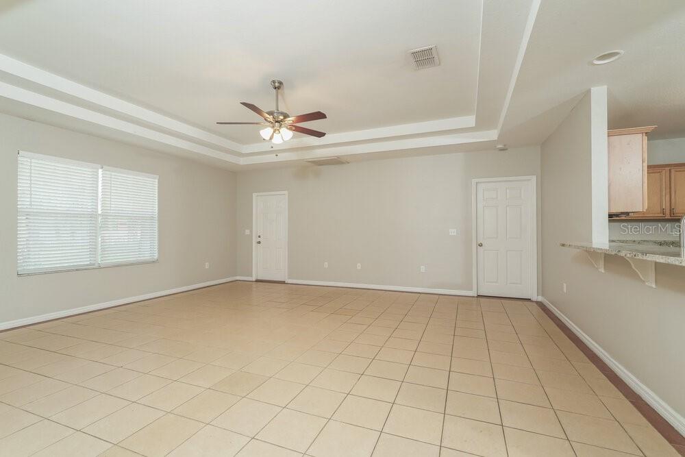 An empty living room features beige tile flooring, a tray ceiling, and two white doors — 6557 SHEPHERD OAKS ROAD, LAKELAND, FL