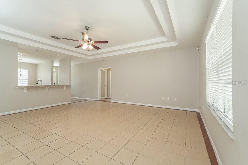 An empty living room with light tile flooring, a ceiling fan, and a breakfast bar — 6557 SHEPHERD OAKS ROAD, LAKELAND, FL