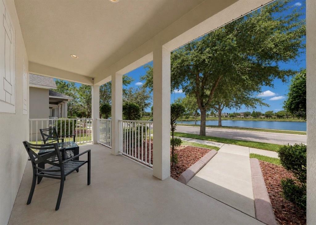 A covered porch with metal chairs overlooks a sidewalk, green lawn, and a small lake — 12020 STREAMBED DRIVE, RIVERVIEW, FL