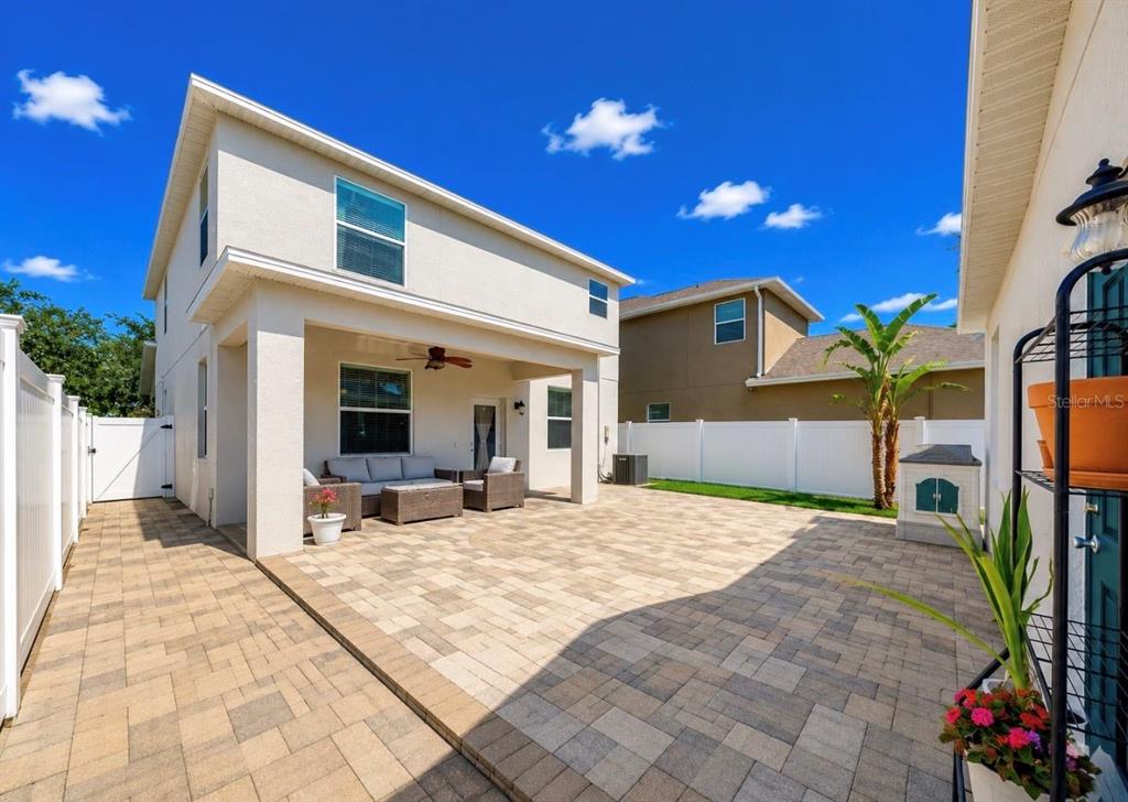 A two-story house exterior with a covered patio, paver flooring, and a white vinyl fence — 12020 STREAMBED DRIVE, RIVERVIEW, FL