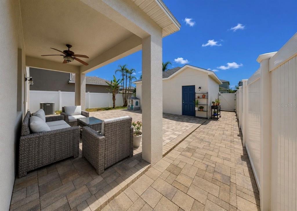 A covered patio with wicker furniture overlooks a paved backyard featuring a detached garage — 12020 STREAMBED DRIVE, RIVERVIEW, FL
