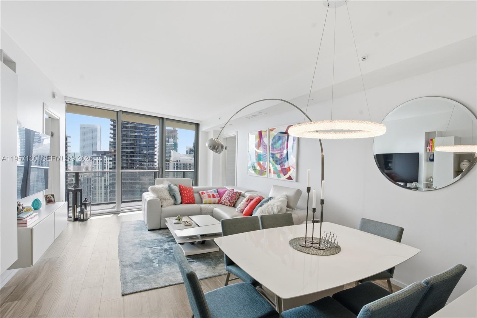 A modern living and dining area features a white sectional, glass table, and city views — 801 S Miami Ave # 4202, Miami FL 33130, MIAMI, FL