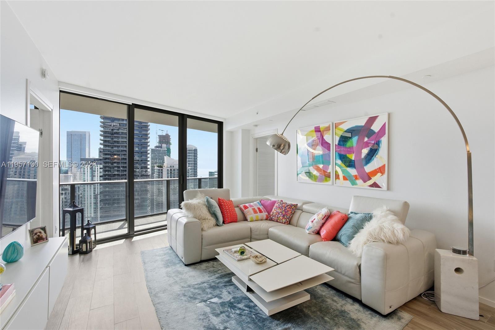 A modern living room features a white sectional sofa, a coffee table, and city views — 801 S Miami Ave # 4202, Miami FL 33130, MIAMI, FL