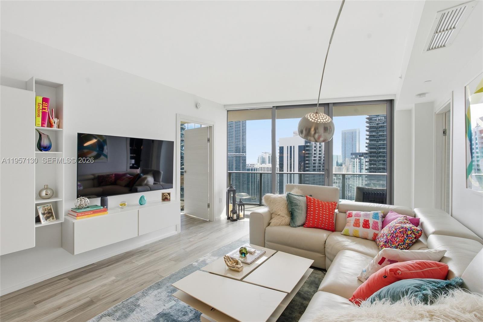 A modern living room features a white sectional sofa, wall-mounted television, and floor-to-ceiling windows — 801 S Miami Ave # 4202, Miami FL 33130, MIAMI, FL