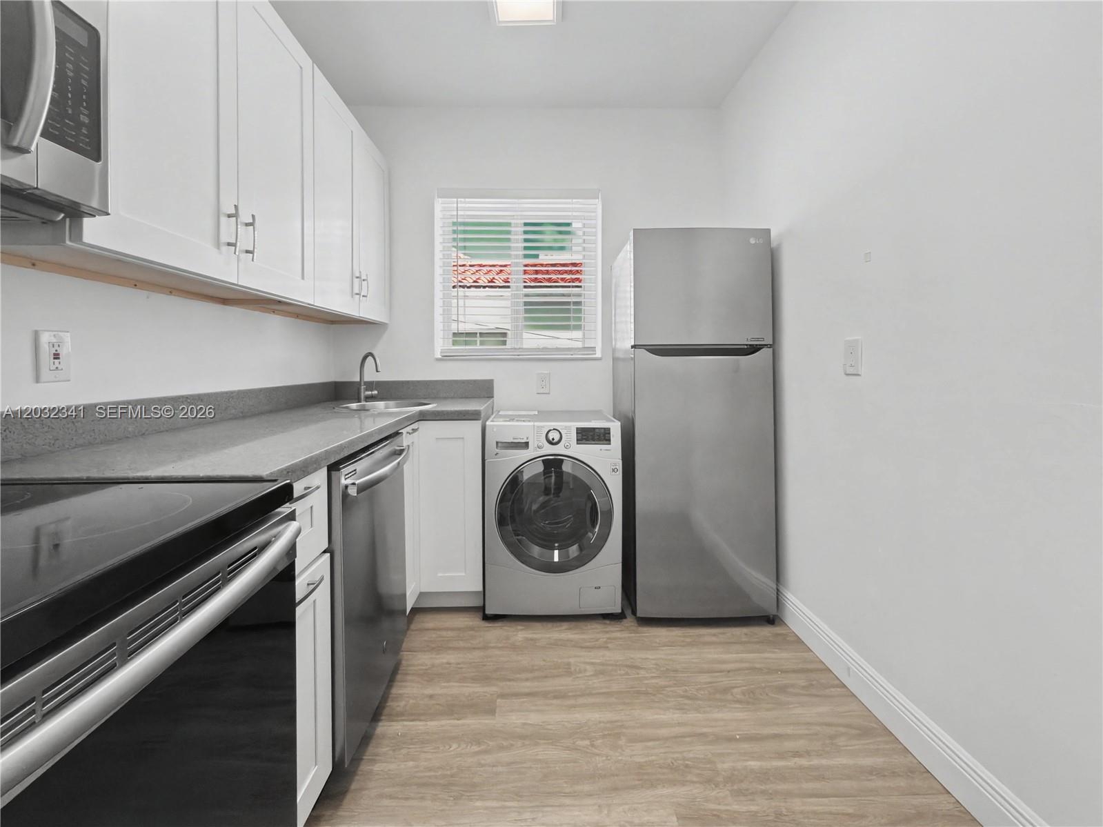 A kitchen features white cabinets, stainless steel appliances, a washer, and light wood flooring — 350 Minorca Ave # 2, Coral Gables FL 33134, CORAL GABLES, FL