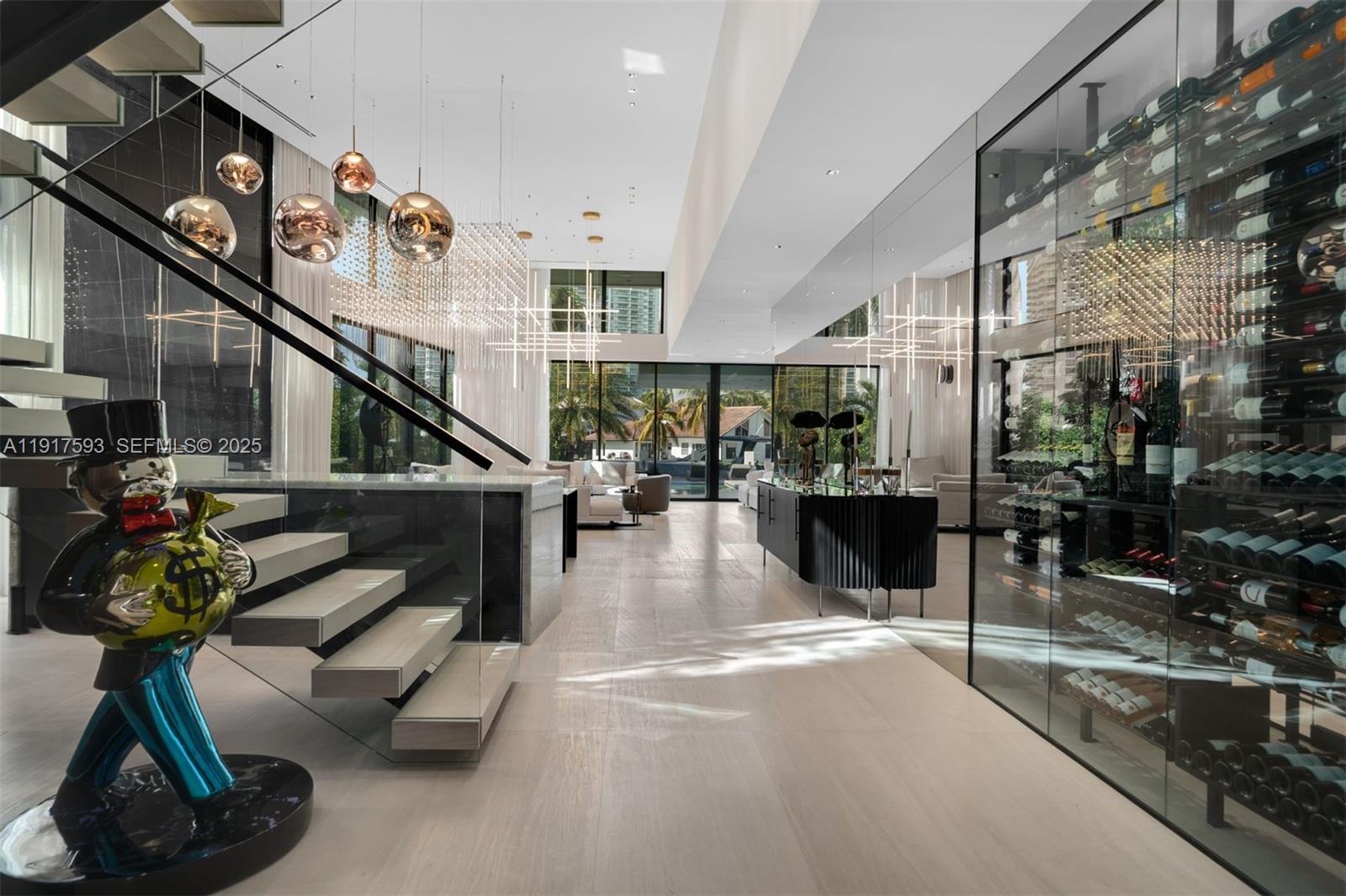 A modern living room features a glass wine cellar, floating staircase, and a Monopoly sculpture — 342 S Parkway, Golden Beach FL 33160, GOLDEN BEACH, FL