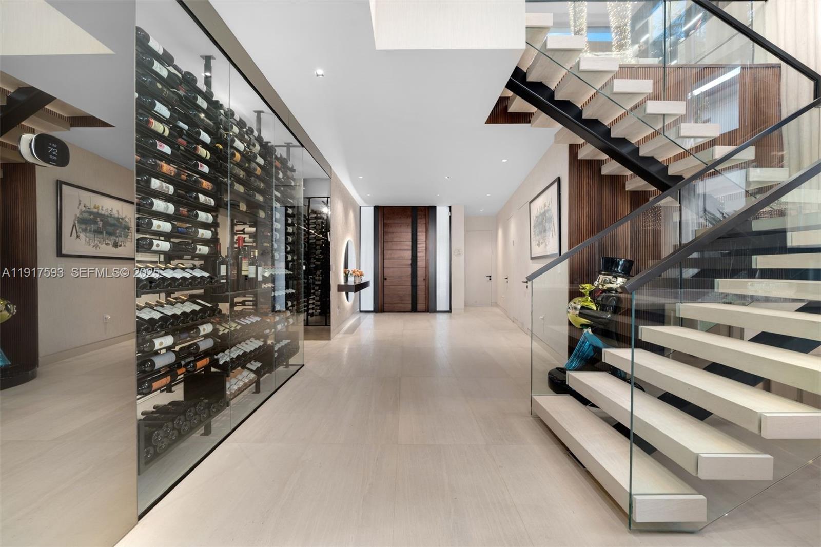 A modern hallway features a glass-enclosed wine cellar, floating staircase, and light-colored tile flooring — 342 S Parkway, Golden Beach FL 33160, GOLDEN BEACH, FL