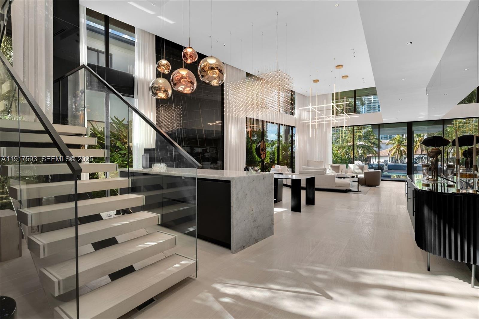 A modern living room features a floating staircase, marble island, and large floor-to-ceiling windows — 342 S Parkway, Golden Beach FL 33160, GOLDEN BEACH, FL