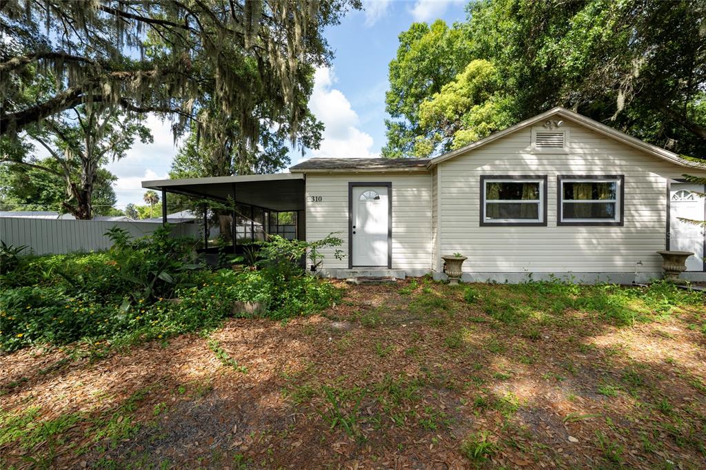 A single-story house with light siding, a covered porch, and a yard with overgrown vegetation — 310 CORDOVA ROAD, AUBURNDALE, FL