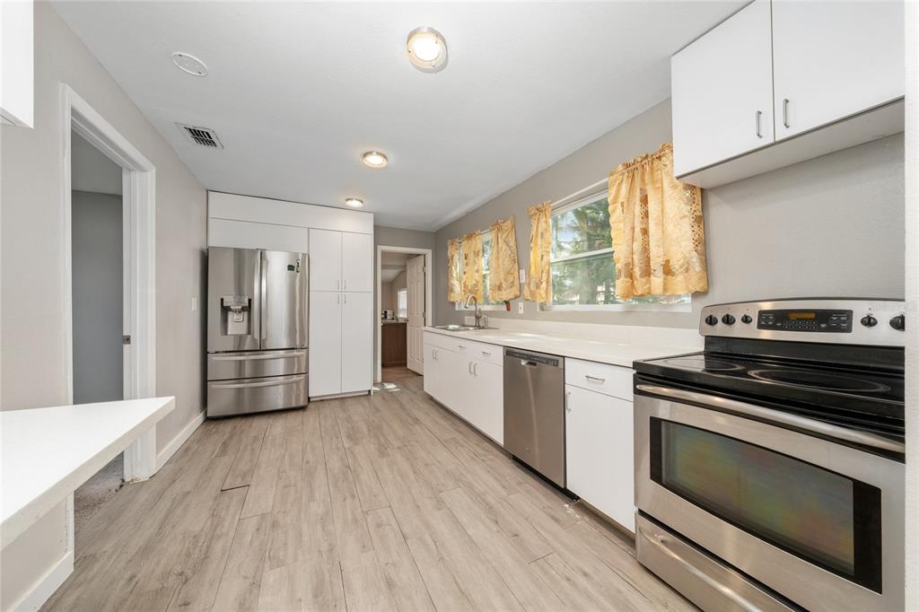 A kitchen features white cabinets, stainless steel appliances, light wood-look flooring, and yellow curtains — 310 CORDOVA ROAD, AUBURNDALE, FL