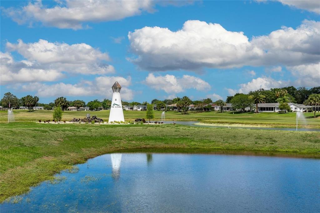 A white lighthouse structure stands near a pond on a golf course with houses nearby — 9498 SE 174TH LOOP, SUMMERFIELD, FL