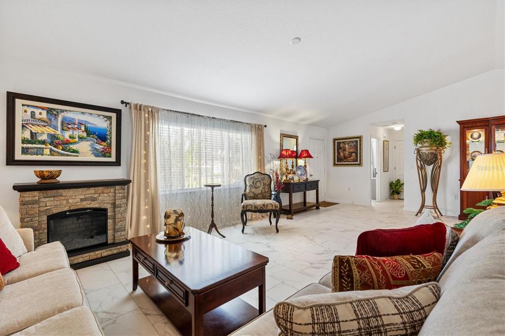 A living room features a stone fireplace, tile flooring, and a large window with curtains — 9498 SE 174TH LOOP, SUMMERFIELD, FL