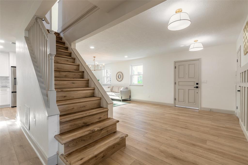 A wooden staircase leads to an upper level in an open-concept living area with light flooring — 82 RAY MAR DRIVE, ORMOND BEACH, FL