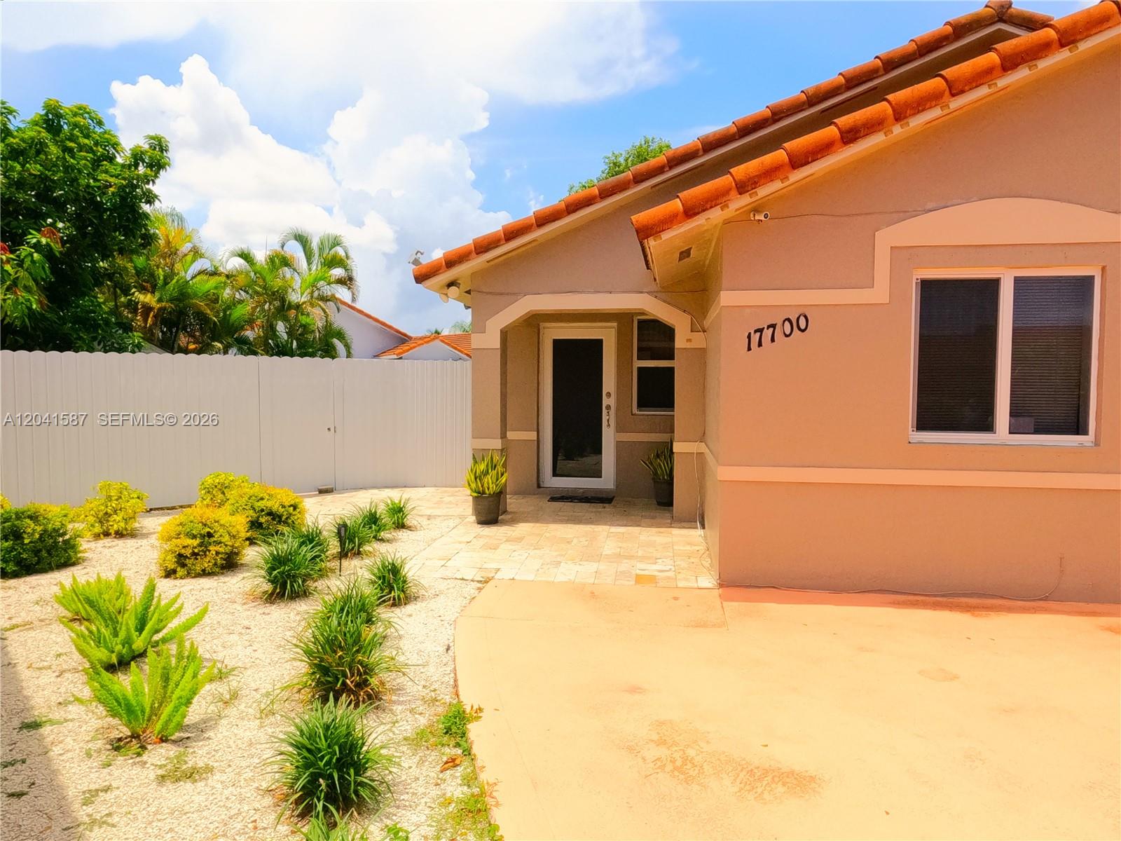 A tan house exterior features a tiled roof, a front entrance, and a gravel yard — 17700 SW 145th Ave, Miami FL 33177, MIAMI, FL