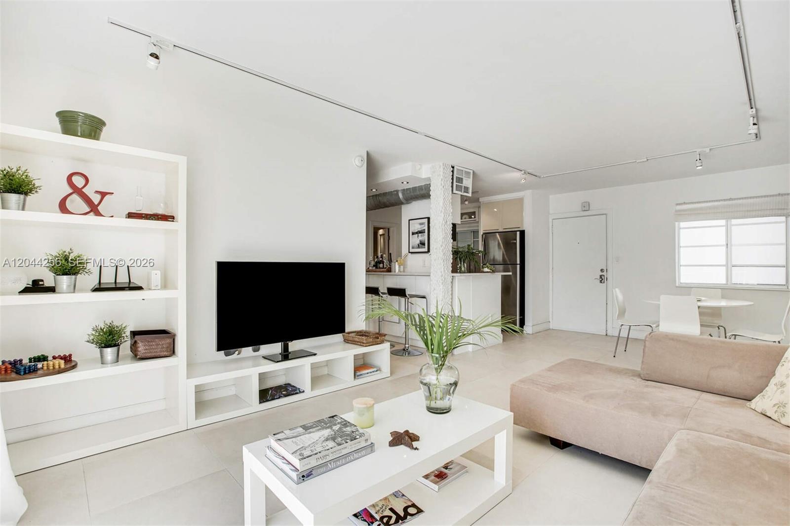 A bright living room features white walls, tile floors, a television, and an open kitchen — 201 Jefferson Ave # 2E, Miami Beach FL 33139, MIAMI BEACH, FL