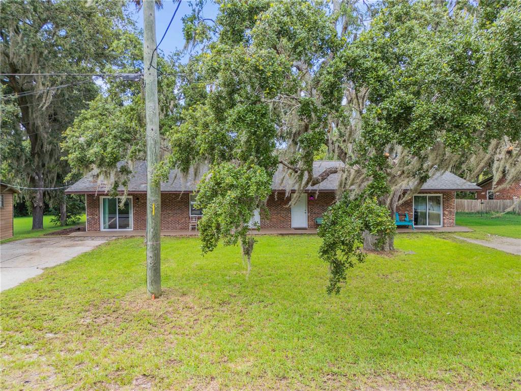 A single-story brick house with a front porch sits behind a large tree and lawn — 1205 16TH STREET, EDGEWATER, FL