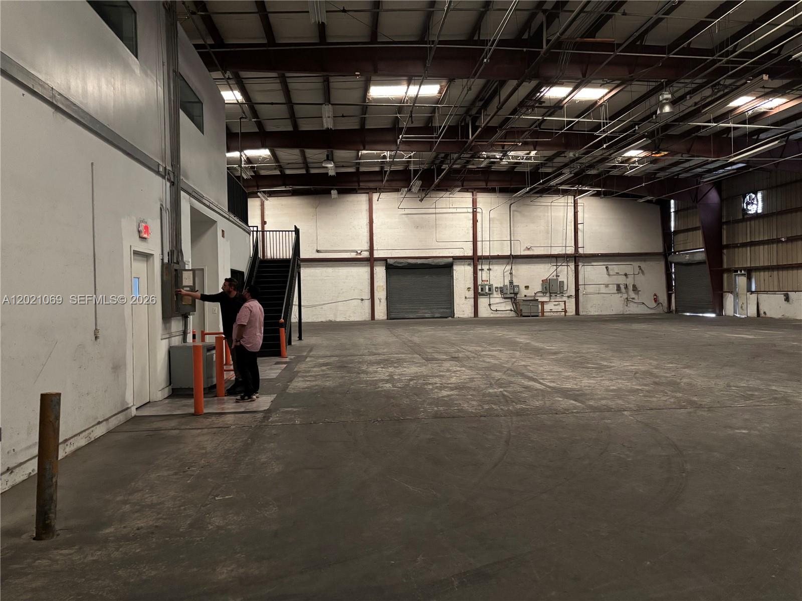 Two people stand near an electrical panel inside a large, open industrial warehouse space — 50 NE 179th St., Miami Gardens FL 33162, MIAMI GARDENS, FL