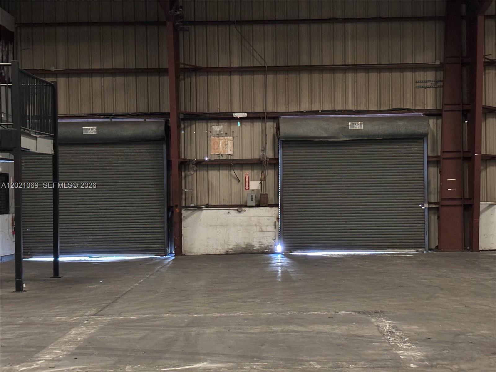 An industrial warehouse interior features two large roll-up metal doors and a concrete floor — 50 NE 179th St., Miami Gardens FL 33162, MIAMI GARDENS, FL