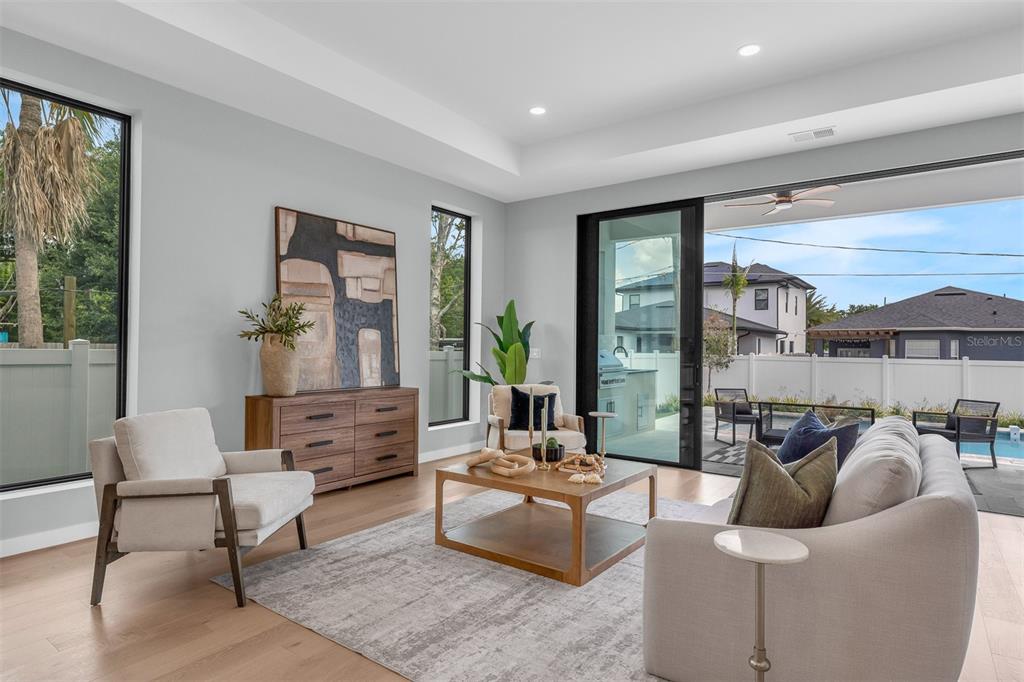 A modern living room features light wood floors, a neutral sofa, and large sliding glass doors — 9 E STEELE STREET, ORLANDO, FL