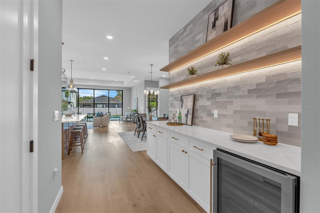 A modern kitchen features white cabinetry, a wine cooler, and floating shelves against tiled walls — 9 E STEELE STREET, ORLANDO, FL