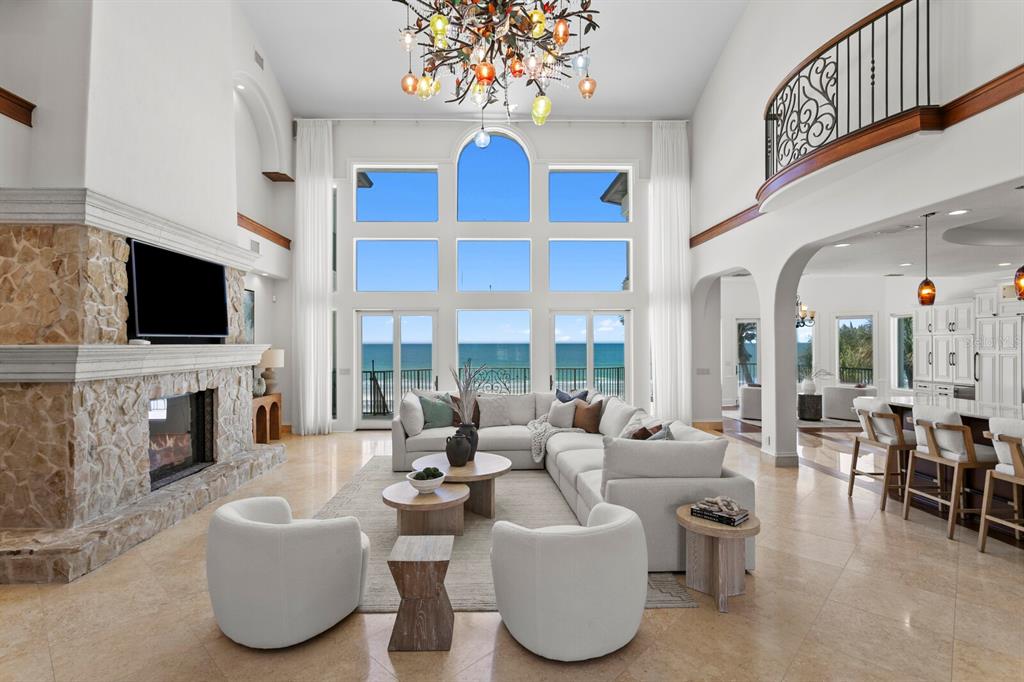 A spacious living room features a stone fireplace, large windows overlooking the ocean, and chandeliers — 15912 GULF BOULEVARD, REDINGTON BEACH, FL