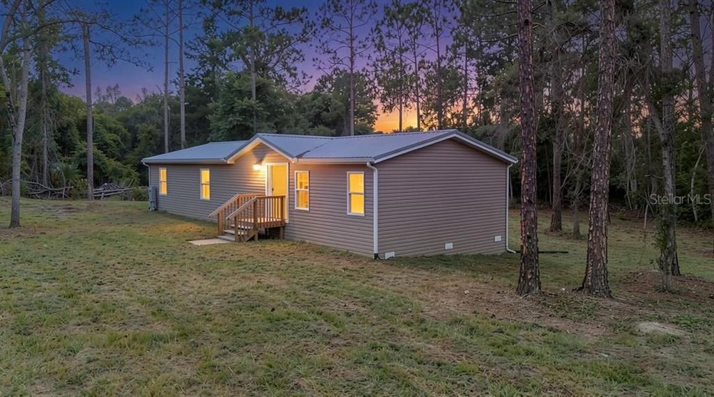 A single-story manufactured home with tan siding sits in a wooded lot at dusk — 44645 TWILIGHT TRAIL, DELAND, FL