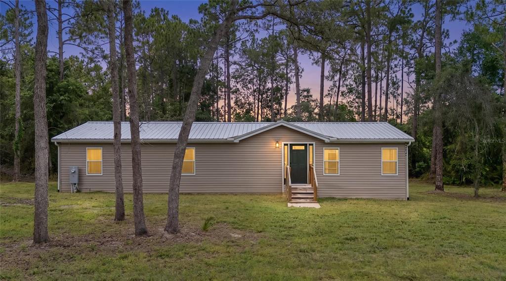 A single-story house with tan siding and a metal roof sits among pine trees — 44645 TWILIGHT TRAIL, DELAND, FL