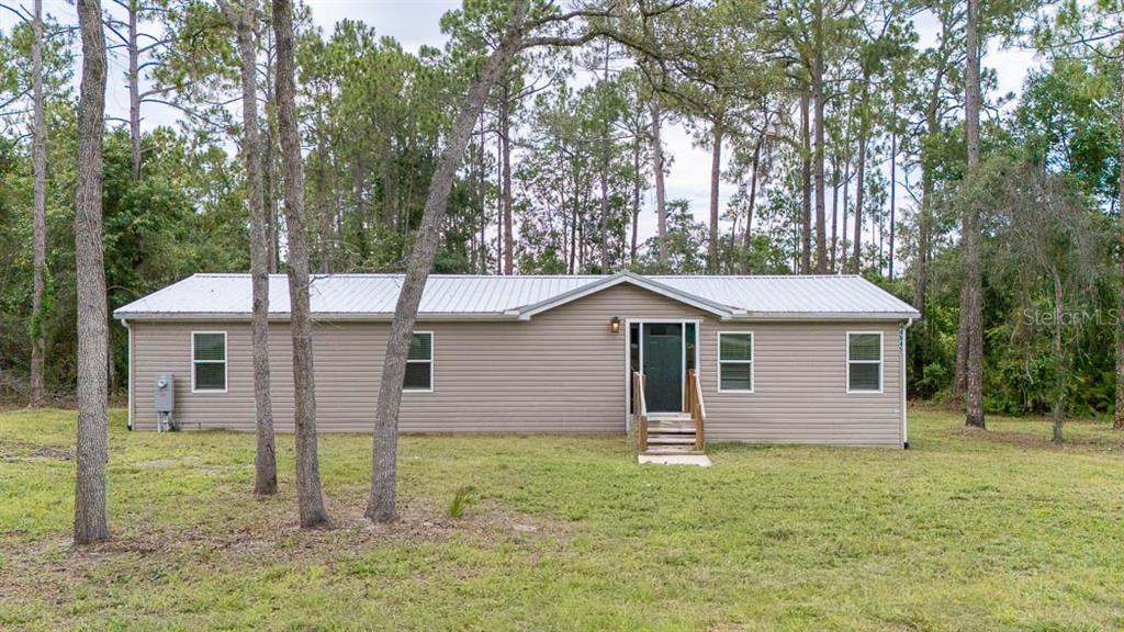 A single-story manufactured home with tan siding and a metal roof sits among trees — 44645 TWILIGHT TRAIL, DELAND, FL