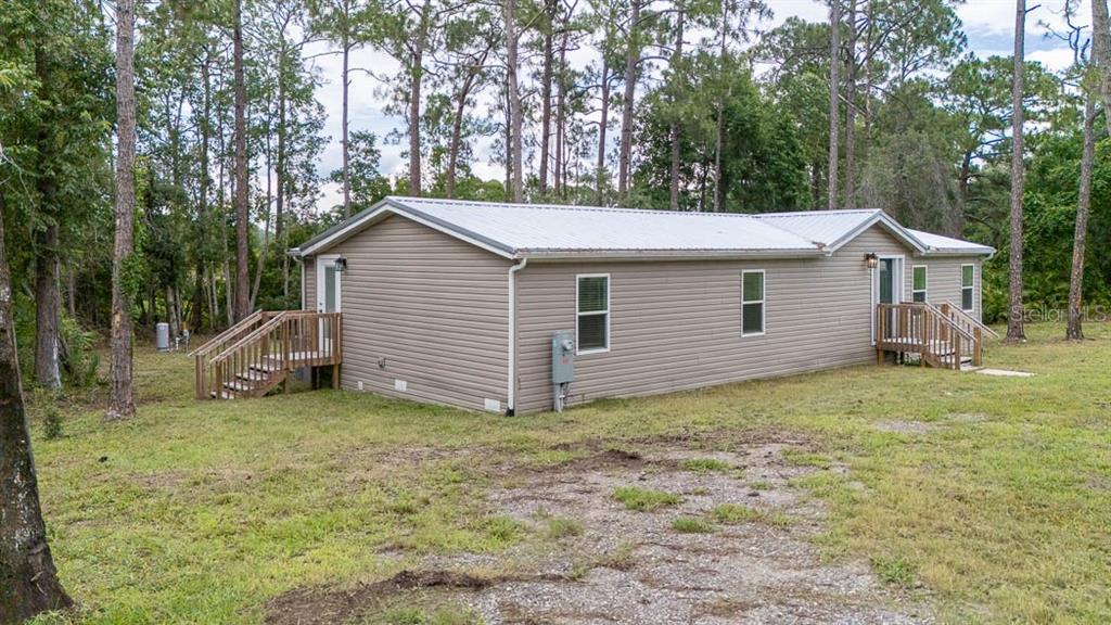 A tan, single-story manufactured home with a metal roof sits on a grassy lot — 44645 TWILIGHT TRAIL, DELAND, FL