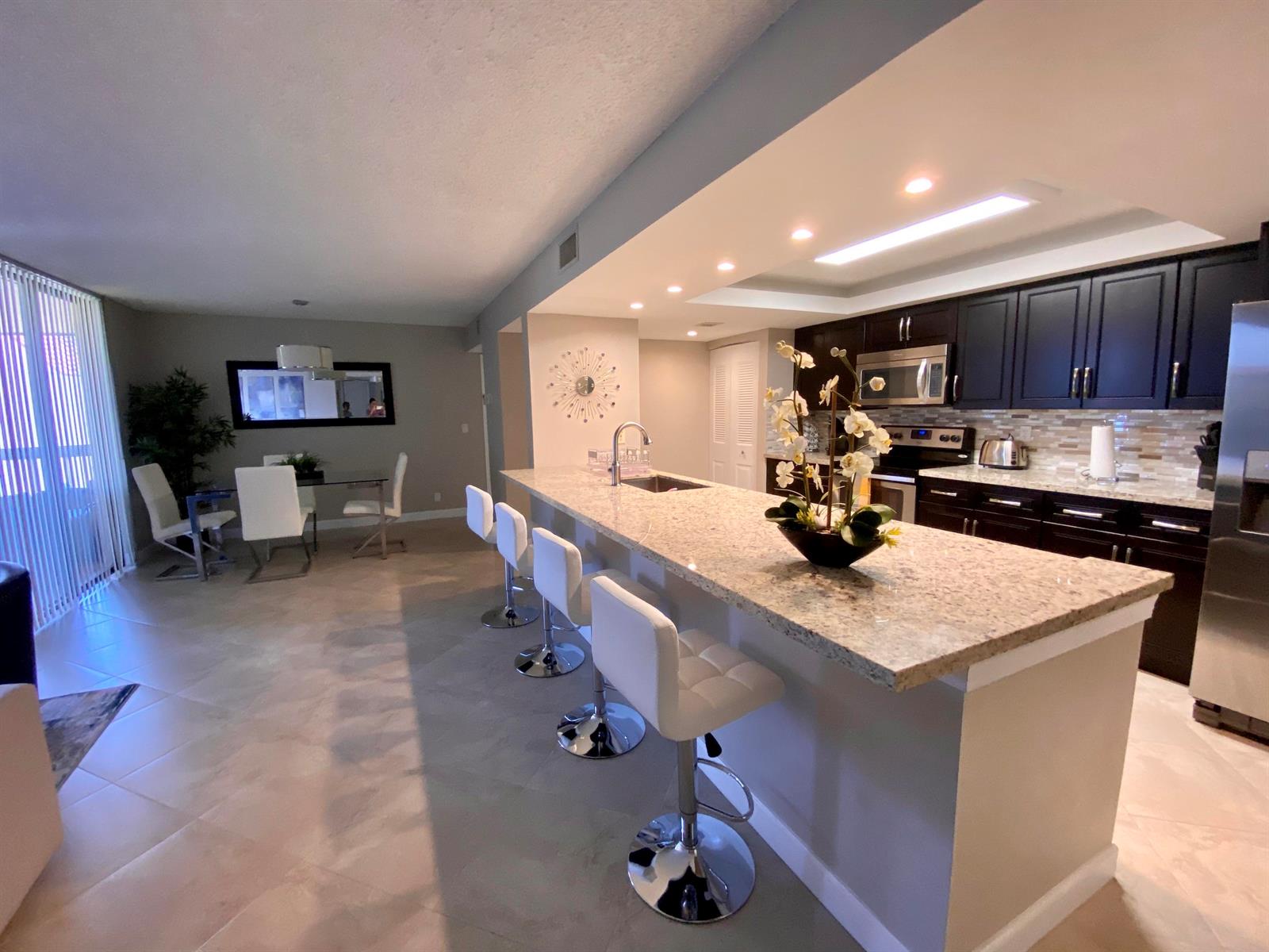 A kitchen with dark cabinets and granite countertops features a breakfast bar with white stools — 2255 Lindell Boulevard Apt 502, Delray Beach FL 33444, DELRAY BEACH, FL