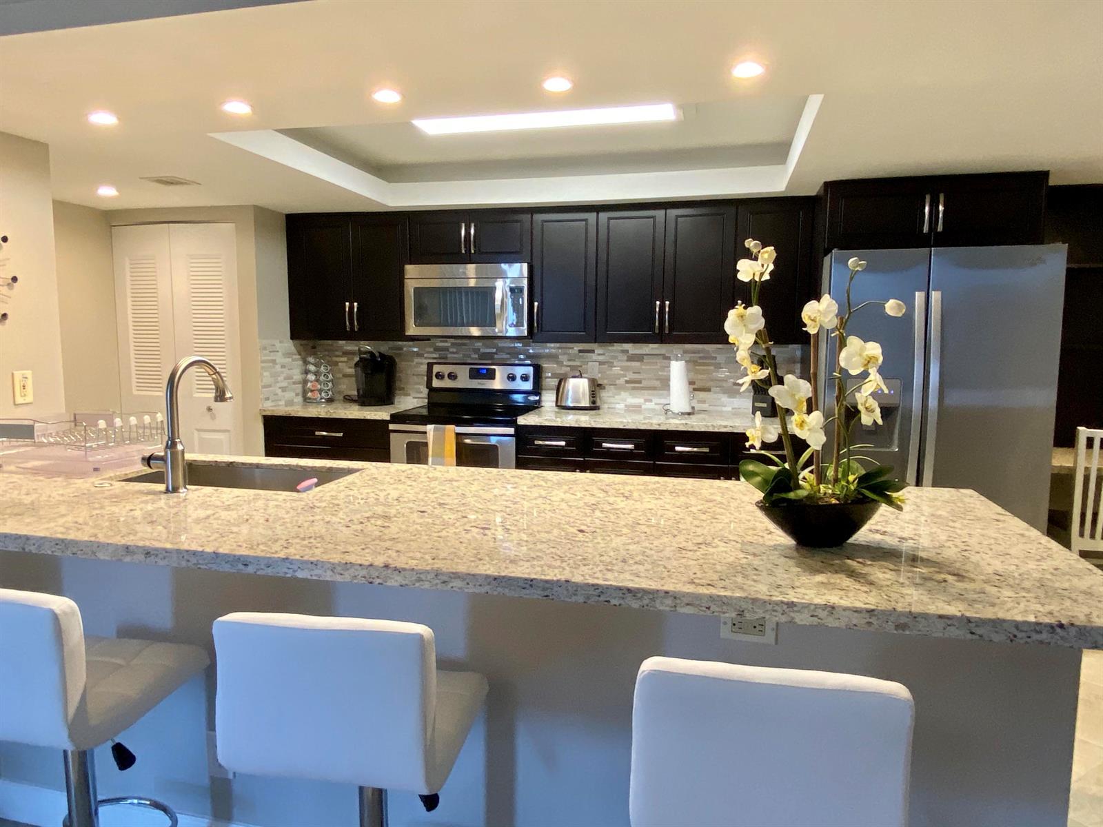 A kitchen features dark cabinetry, granite countertops, stainless steel appliances, and a breakfast bar — 2255 Lindell Boulevard Apt 502, Delray Beach FL 33444, DELRAY BEACH, FL