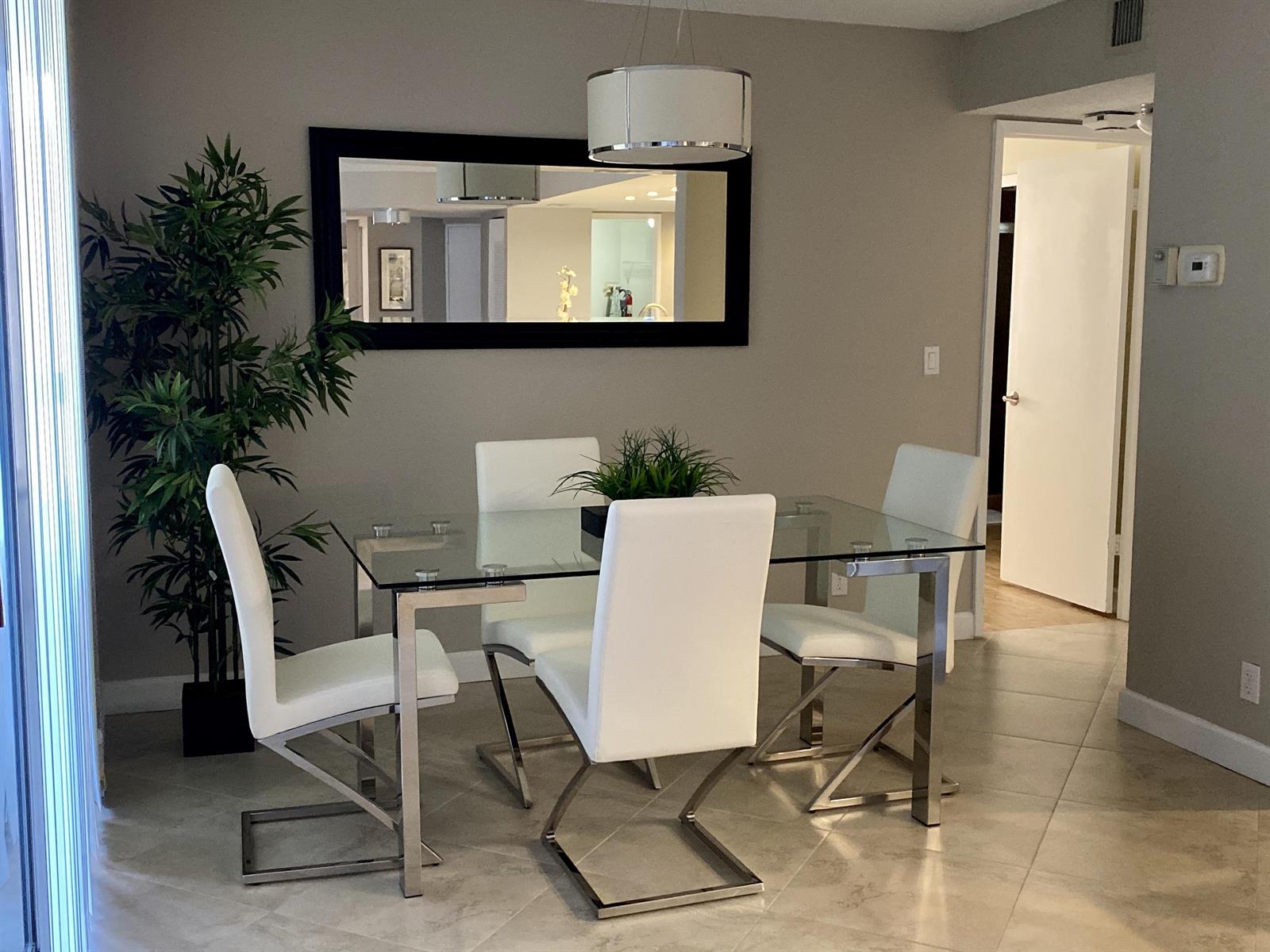 A dining room features a glass-topped table, four white chairs, and a large wall mirror — 2255 Lindell Boulevard Apt 502, Delray Beach FL 33444, DELRAY BEACH, FL