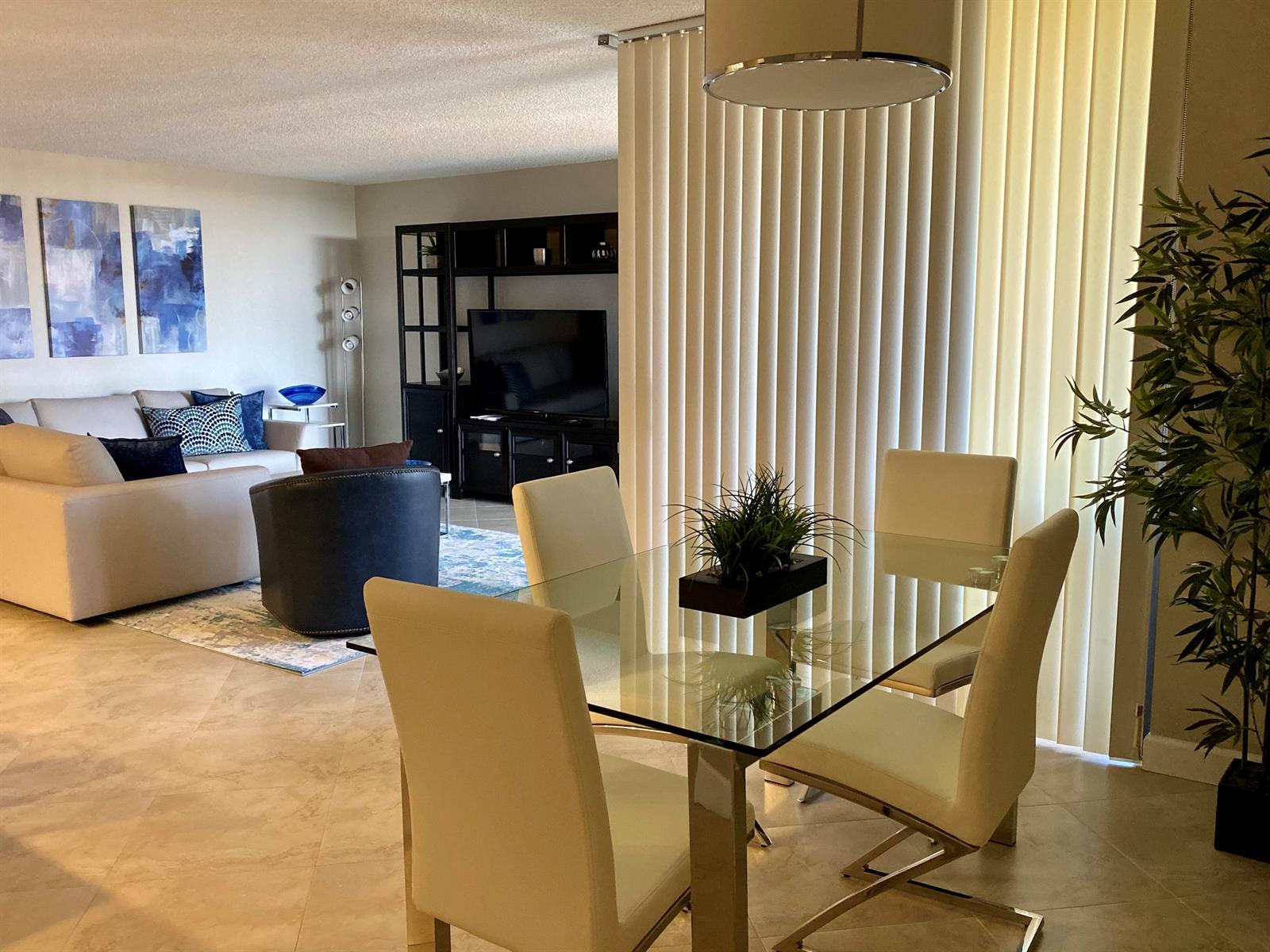A dining area with a glass table and chairs sits in front of a living room — 2255 Lindell Boulevard Apt 502, Delray Beach FL 33444, DELRAY BEACH, FL
