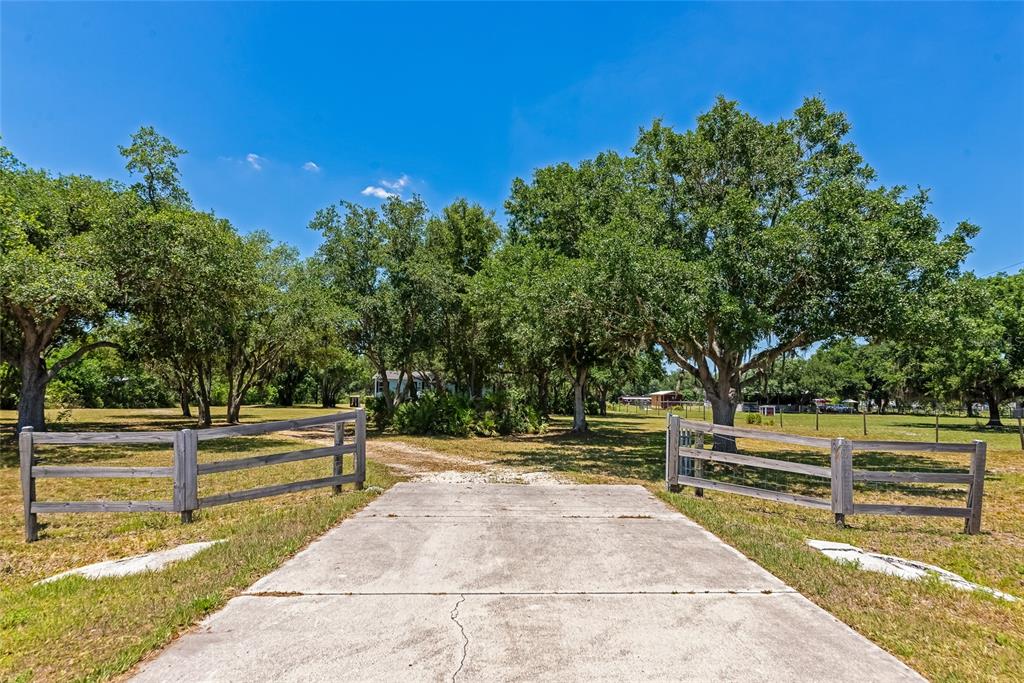 A concrete driveway leads through a wooden fence toward a tree-lined property — 14110 SUGAR BOWL ROAD, MYAKKA CITY, FL