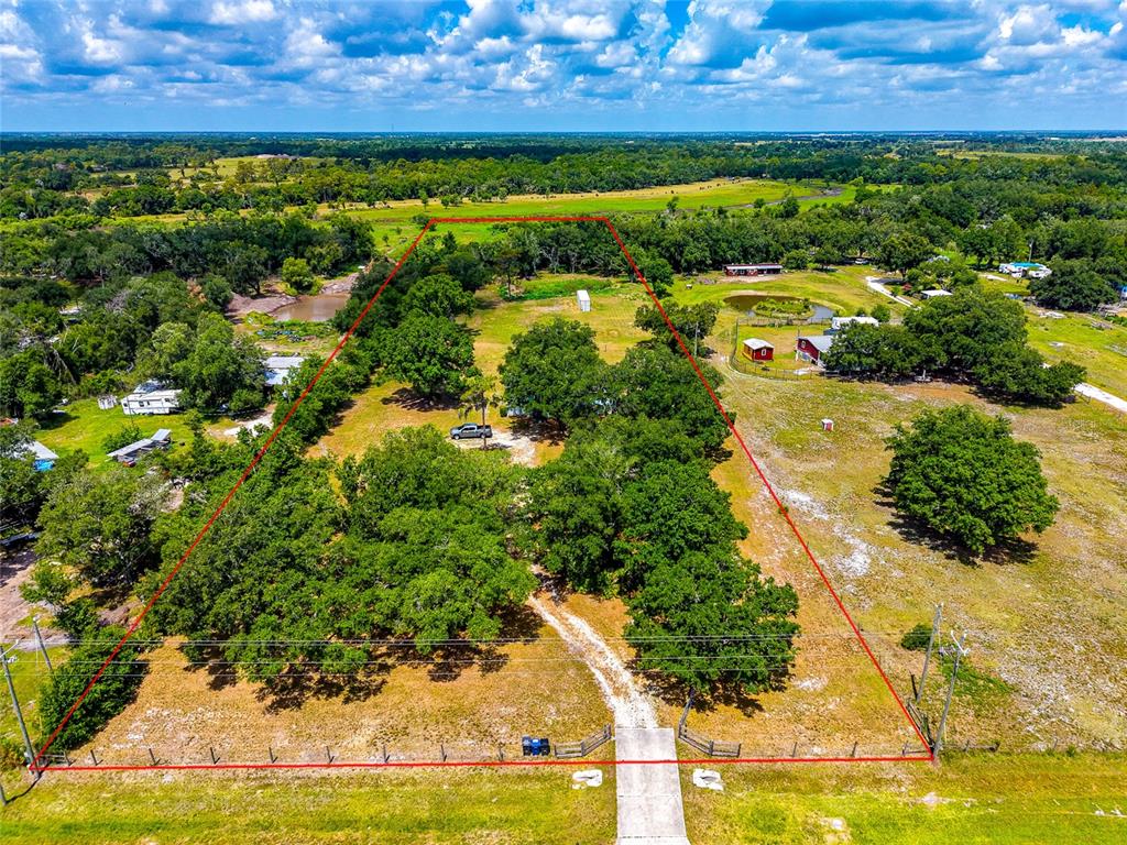 An aerial view shows a fenced, tree-filled rural lot with a gravel driveway and structures — 14110 SUGAR BOWL ROAD, MYAKKA CITY, FL