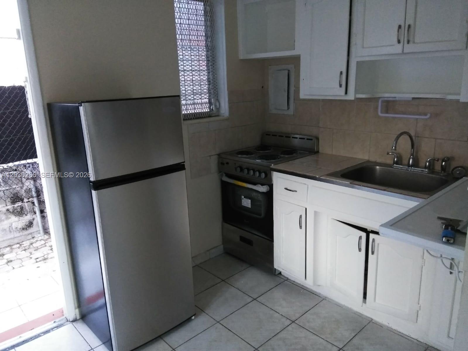 A small kitchen features white cabinets, a stainless steel refrigerator, a stove, and tiled flooring — 1821 SW 7th St # 7, Miami FL 33135, MIAMI, FL