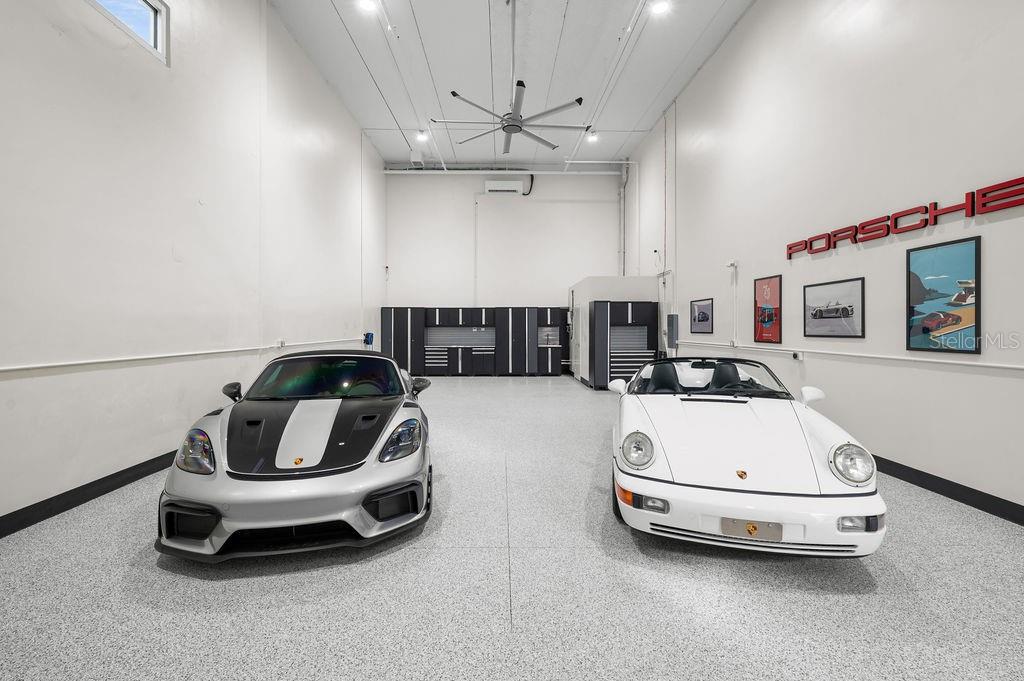 A high-ceilinged garage with epoxy flooring houses a silver sports car and a white Porsche — 5431 COMMUNICATIONS PARKWAY UNIT 28, LAKEWOOD RANCH, FL