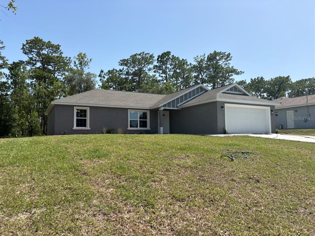 A gray, single-story house with a white garage door sits on a grassy lot — 1854 W CARY DRIVE, DUNNELLON, FL