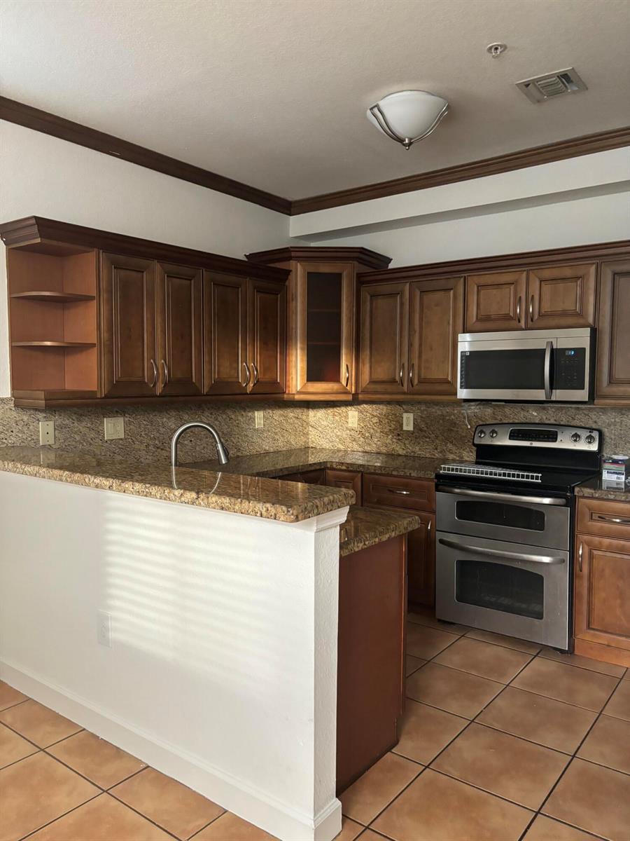 A kitchen features dark wood cabinets, granite countertops, stainless steel appliances, and tile flooring — 4311 SW 160th Avenue # 210, Miramar FL 33027, MIRAMAR, FL