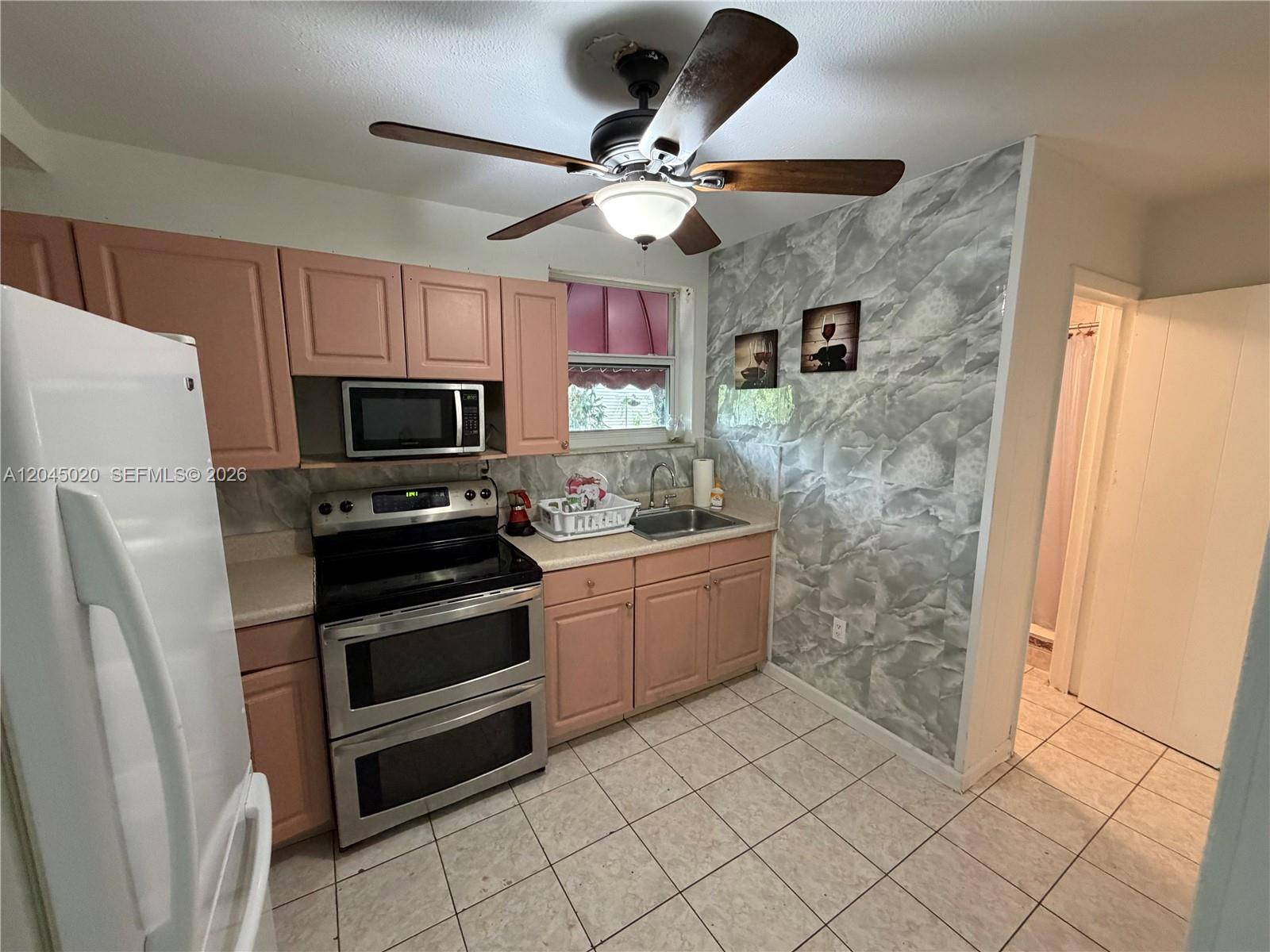 A kitchen features pink cabinets, stainless steel appliances, and a gray faux-marble accent wall — 4935 SW 101st Ave # 1, Miami FL 33165, MIAMI, FL