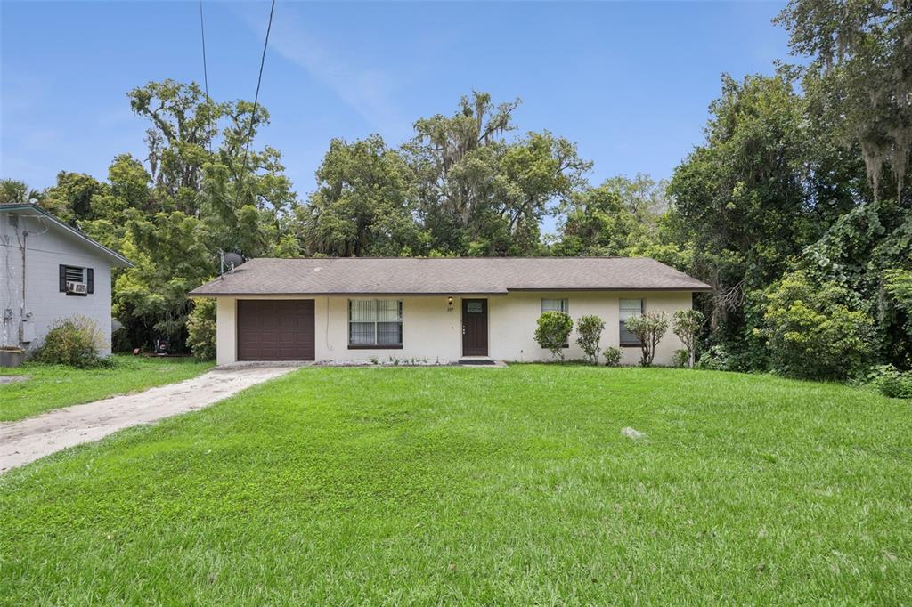 A single-story house with a brown garage door, tan exterior, and a large front lawn — 397 S ORANGE AVENUE, ORANGE CITY, FL
