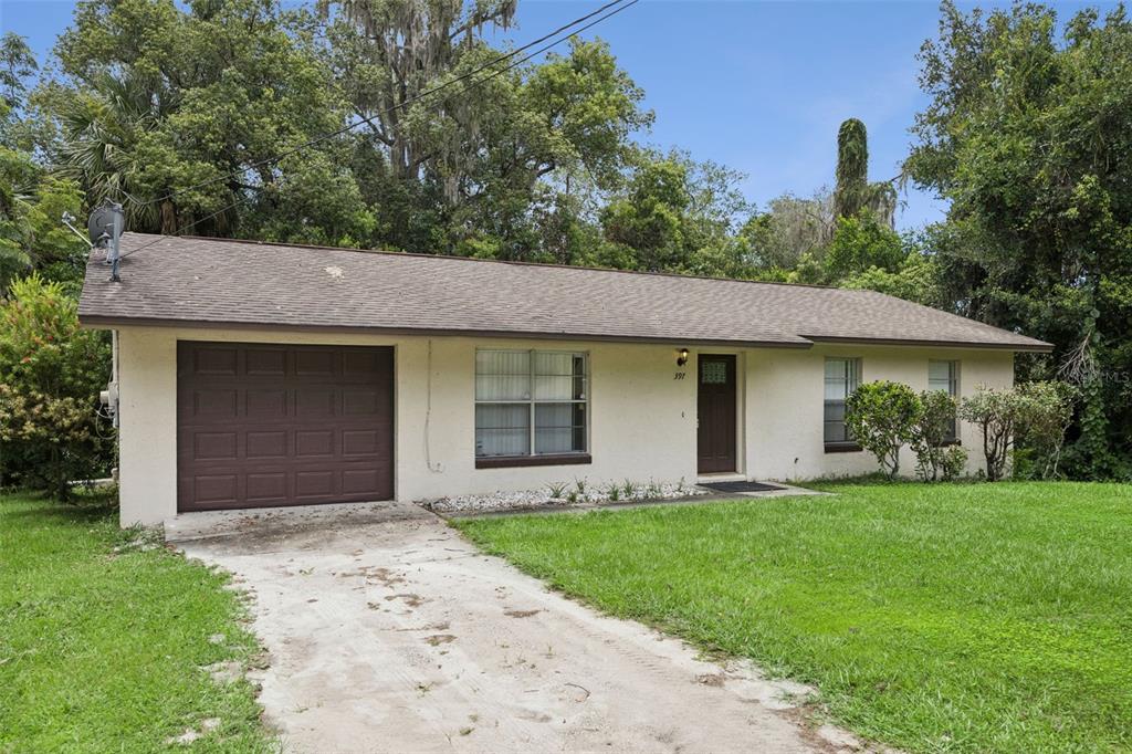 A single-story house with a beige stucco exterior, brown garage door, and a concrete driveway — 397 S ORANGE AVENUE, ORANGE CITY, FL