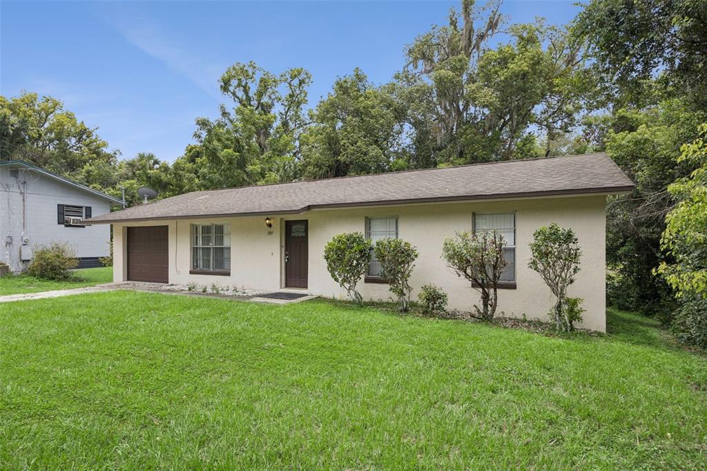 A single-story house with a beige stucco exterior, a brown roof, and a small garage — 397 S ORANGE AVENUE, ORANGE CITY, FL