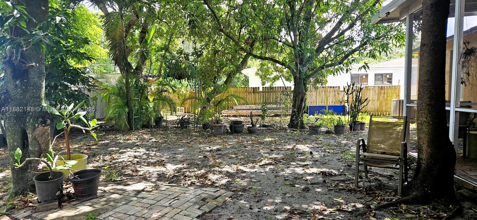A backyard features a sandy ground, scattered potted plants, mature trees, and a wooden fence — 243 NW 62nd Ct, Miami FL 33126, MIAMI, FL